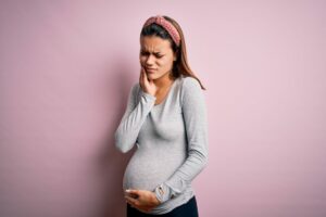 Pregnant mother contemplating wisdom teeth removal during pregnancy while holding her jaw
